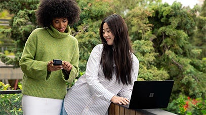 Two people collaborating outdoors using a smartphone and laptop.