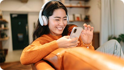 ヘッドフォンを装着し、オレンジ色のソファに座り、携帯電話を使用している人。