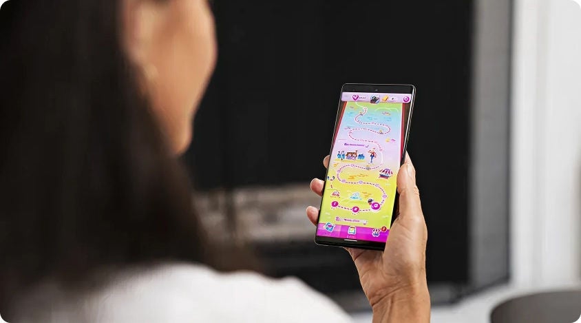 Person holding a smartphone, which is open to a colorful winding map, and playing Candy Crush Saga 