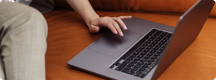 Person sitting on a brown leather couch using a laptop, with one hand on the trackpad.